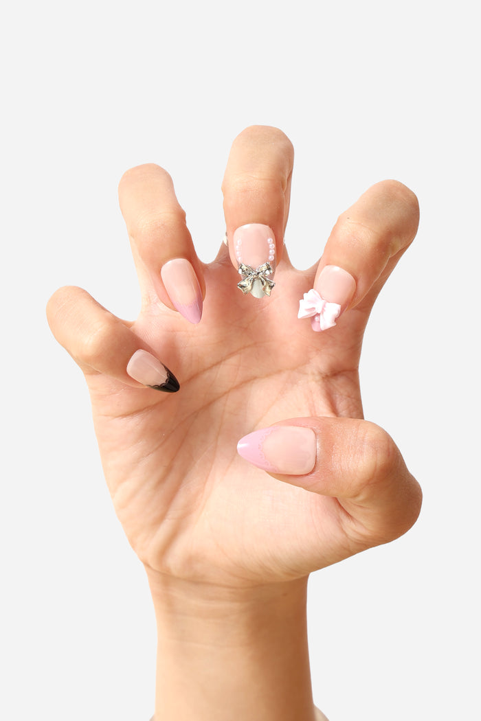 Short almond press-on nails with delicate lace, pink bows, pearls, and metallic accents.