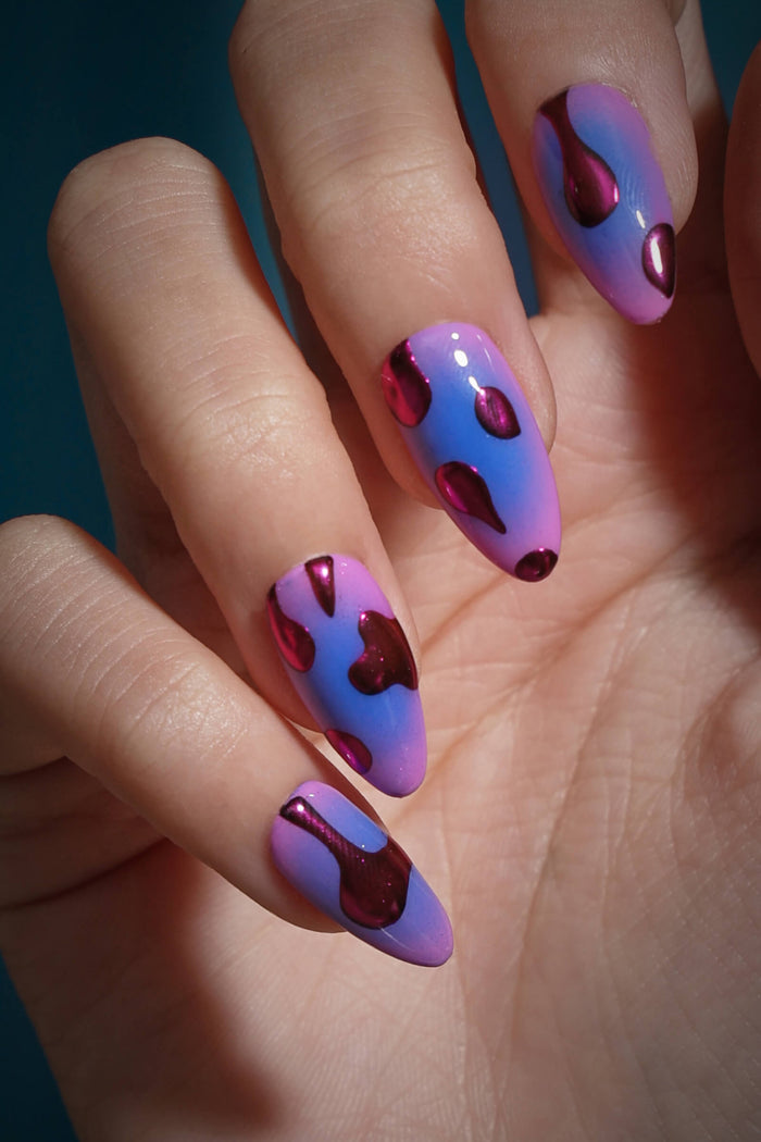 Almond press-on nails with a gradient of pink and blue, featuring metallic deep red "lava" blobs.