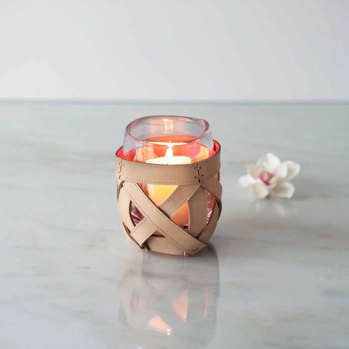 Tan leather wrap with cutout details around a glass candle holder containing red and yellow layers.