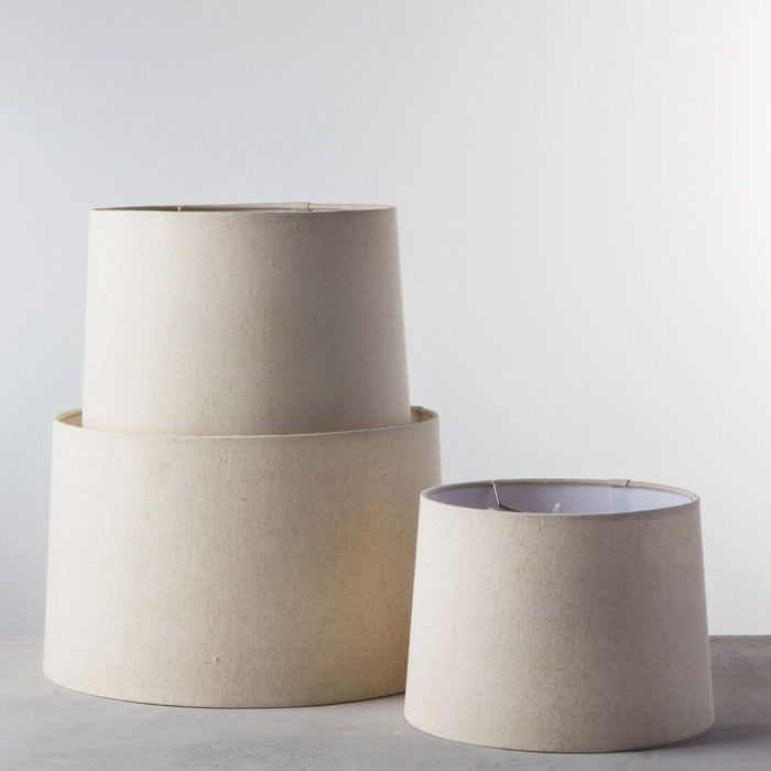Three natural linen barrel lamp shades in graduated sizes with metal trim, displayed stacked and separately.
