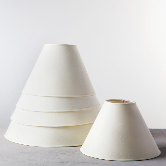 Cream linen empire lampshades in two sizes, displayed side by side on gray surface.