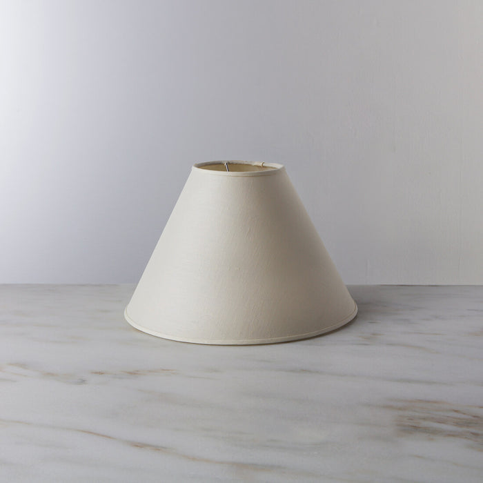 Cream-colored linen empire lamp shade with brass trim, tapered cone shape.