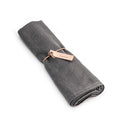 Grey linen table runner rolled and tied with a rose gold band.