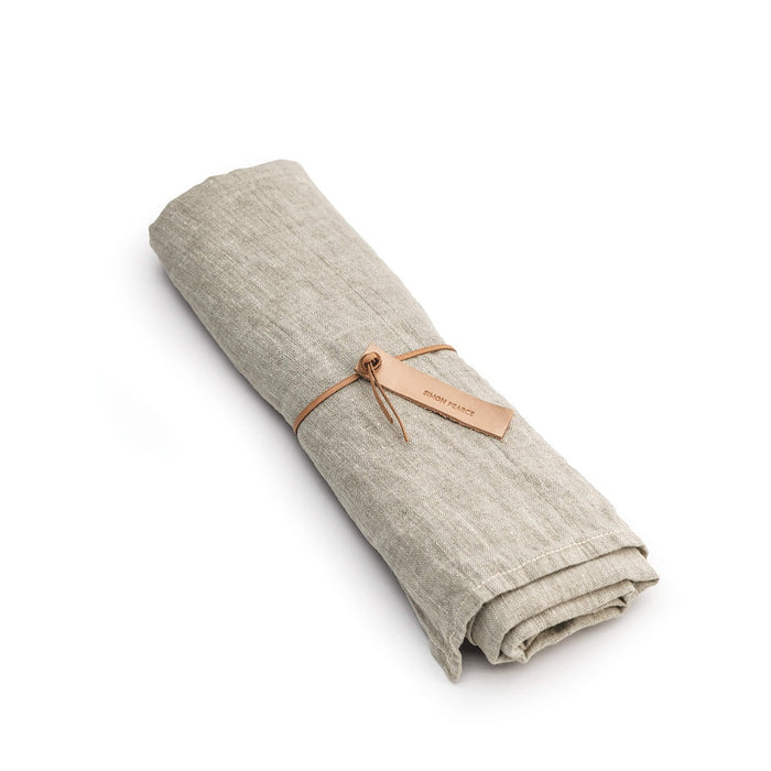Natural linen table runner rolled and tied with a tan leather strap and label.