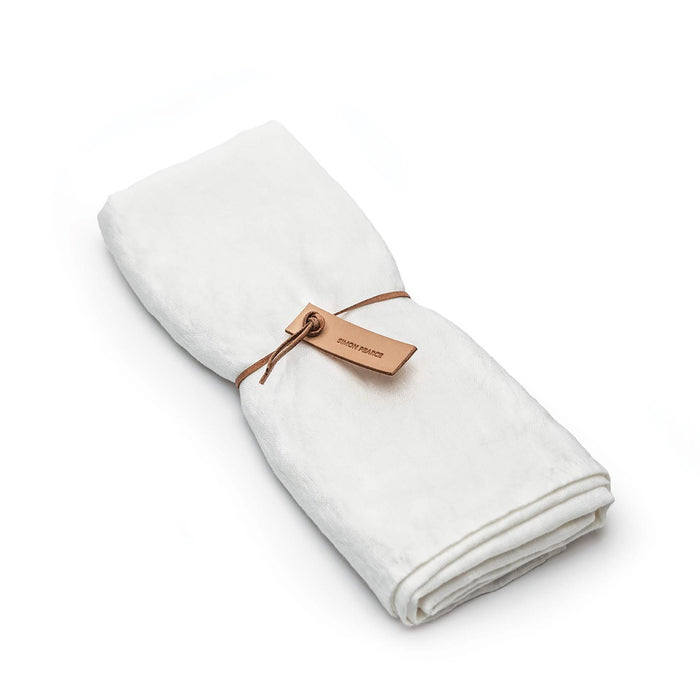 White linen table runner rolled and tied with a tan leather tag and cord.