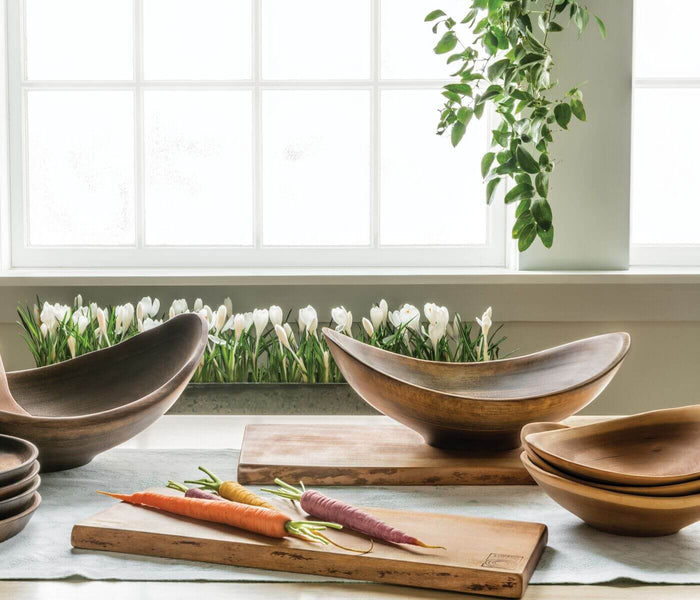 Black walnut wooden bowls with irregular live edges displayed on windowsill with cutting boards and vegetables.