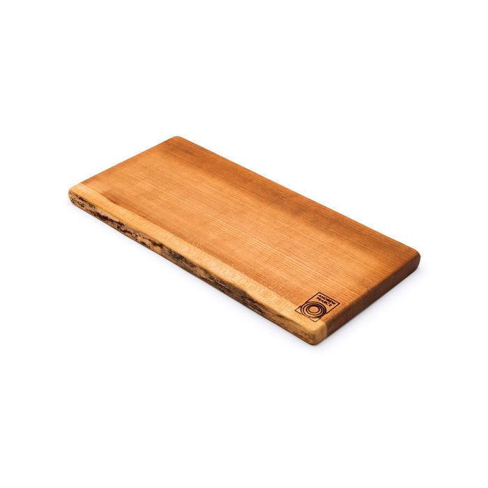 Cherry wood serving board with natural live edge, angled view showing warm grain and bark detail on long side.