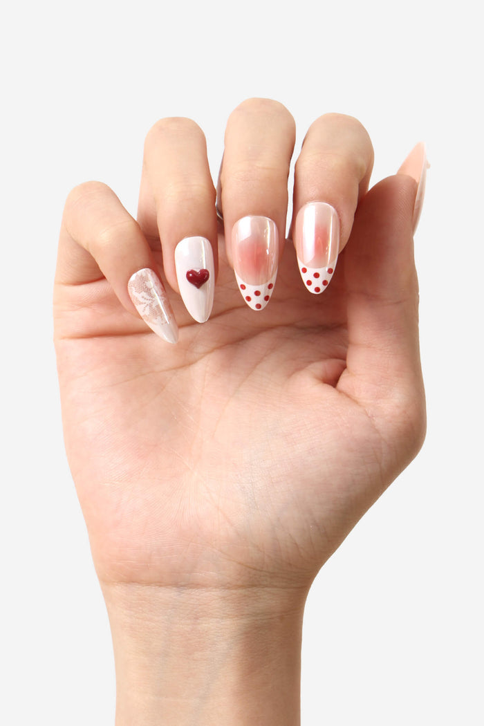 Almond press-on nails featuring a white base with a red heart, lace pattern, and red polka dots.