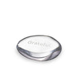 Clear glass stone with "Grateful" engraved on top surface and dark gray curved edges.