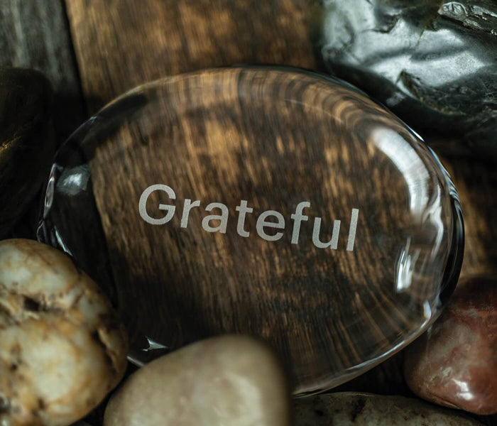 Polished stone with wood grain pattern engraved with the word "Grateful" surrounded by smaller rocks.