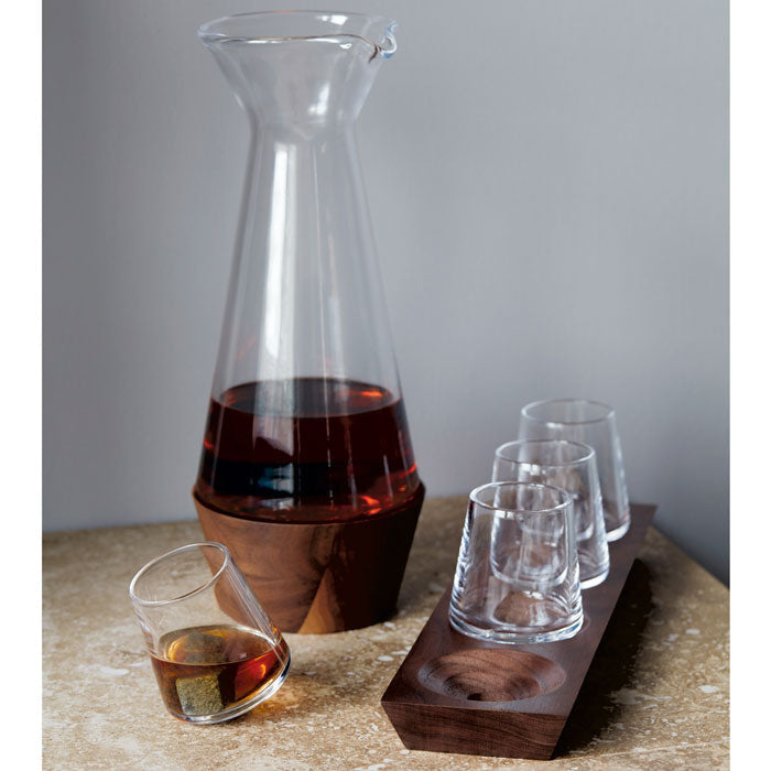 Four clear whiskey glasses with wood base holder and matching glass decanter containing amber liquid.