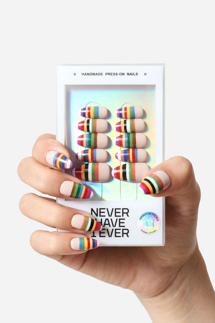 Hand showcasing beige press-on nails with colorful striped design, package reads 'Never Have I Ever' and 'Amber Vittoria'.
