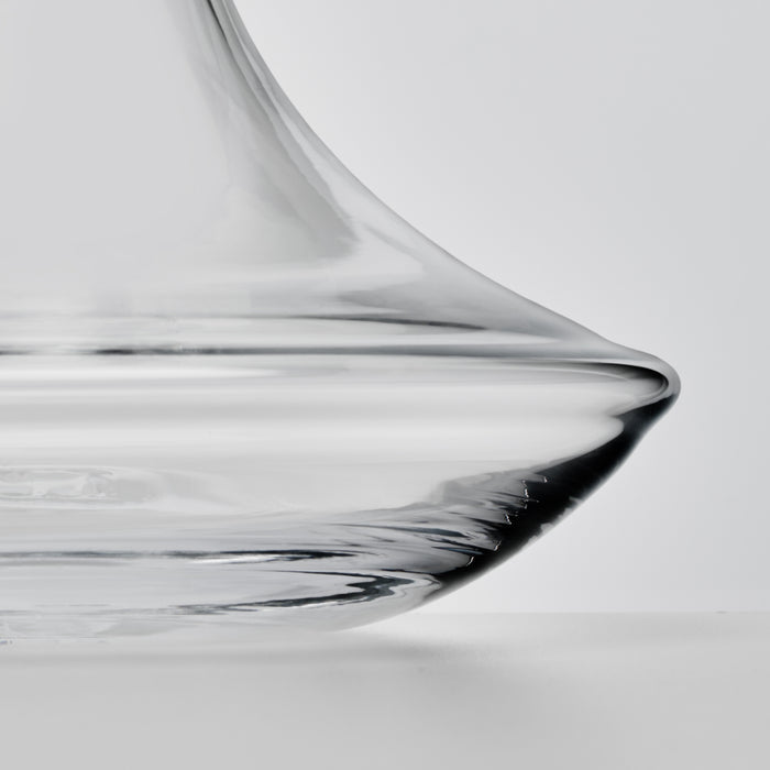 Clear glass wine decanter with curved spout and wide base, shown in close-up detail against neutral background.