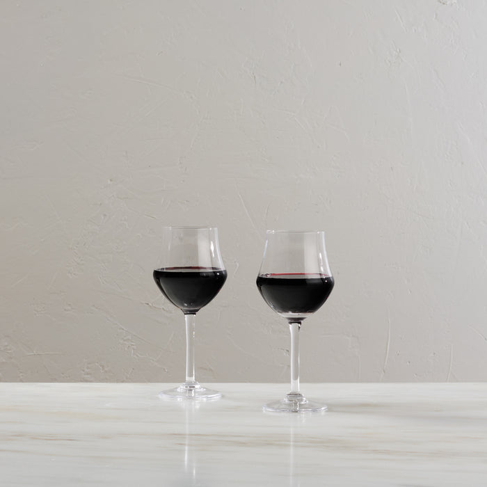 Two clear wine glasses filled with red wine on a white surface against a textured white background.