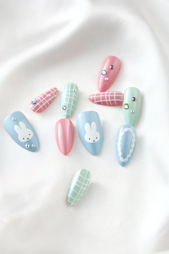 Pastel almond press-on nails featuring Miffy designs, plaid patterns, and rhinestones.