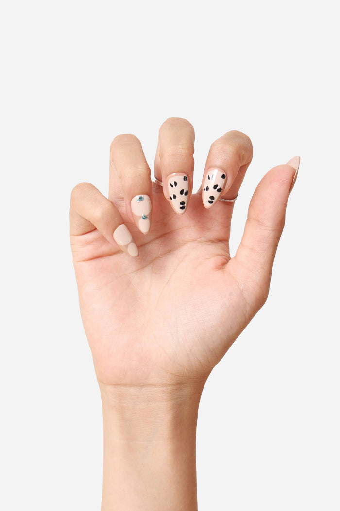Short almond press-on nails with a neutral base, polka dot accents, and rhinestone embellishments.