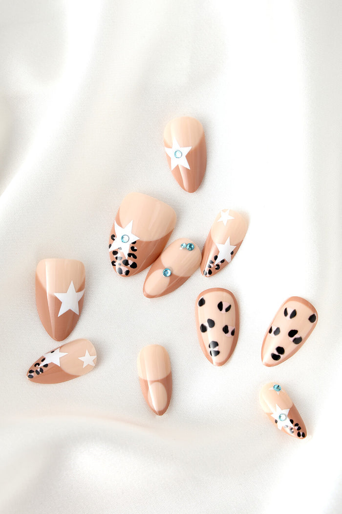 Short almond press-on nails, mocha & nude with stars, dots, and rhinestones. Never Have I Ever branding.