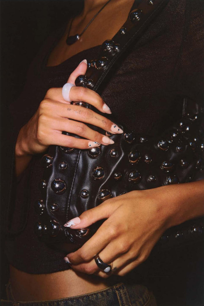 Hands with animal print star press-on nails hold black studded bag.