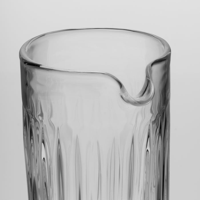Clear glass pitcher with vertical ribbed texture and curved pouring spout.