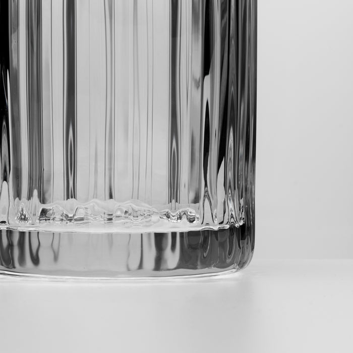 Clear glass pitcher with vertical ribbed texture and rounded base, shown in close-up detail against white background.