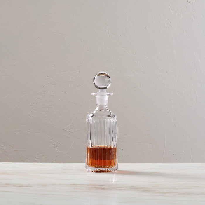 Clear glass decanter with vertical ribbed pattern, spherical stopper, filled with amber liquid.