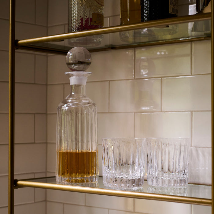 Clear glass decanter with spherical stopper and vertical ribbed pattern, displayed with two matching glasses containing amber