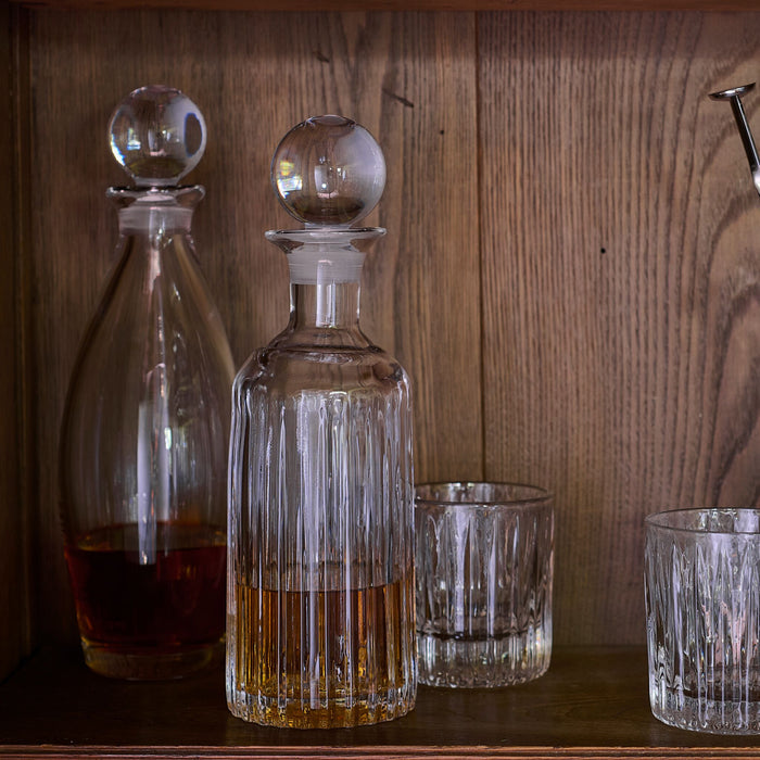 Clear glass decanter with spherical stopper and vertical fluting, displayed with matching glasses containing amber liquid.