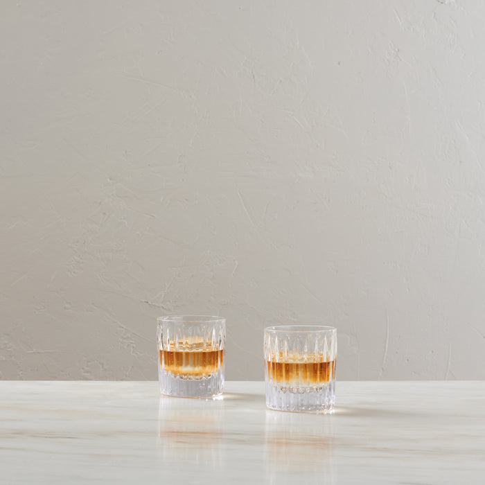 Two crystal double old-fashioned glasses with amber liquid and cut pattern design on white surface.