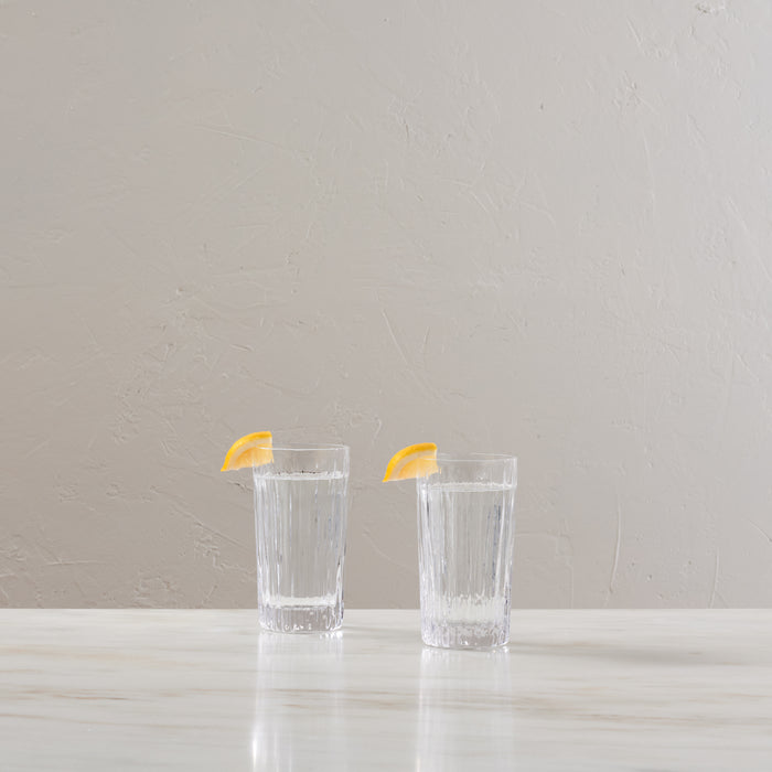 Two clear highball glasses with vertical ribbed texture, each garnished with a lemon slice.