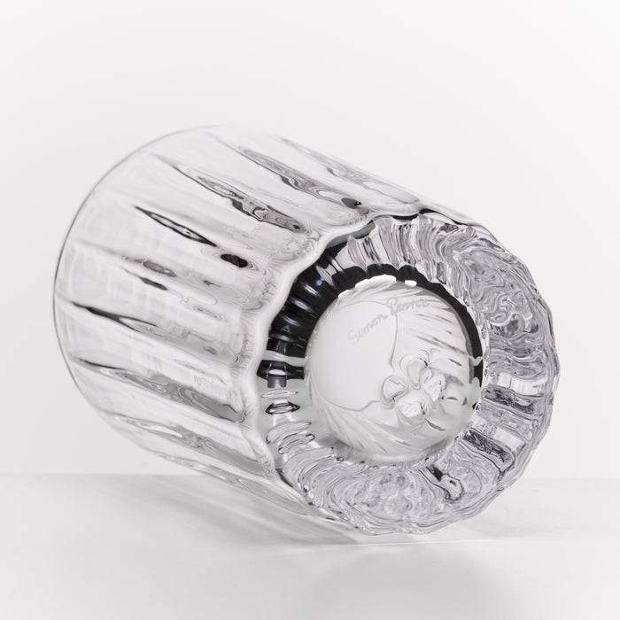 A clear cut-glass tumbler with a ribbed fluted body and a patterned circular base, photographed on a clean white background.