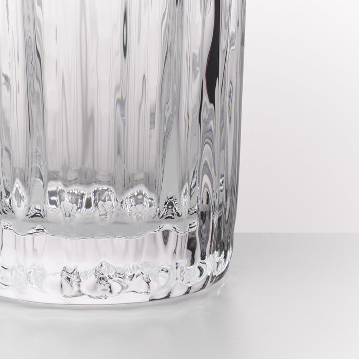 Close-up of a clear ribbed glass tumbler with a textured base, shown against a plain white background.