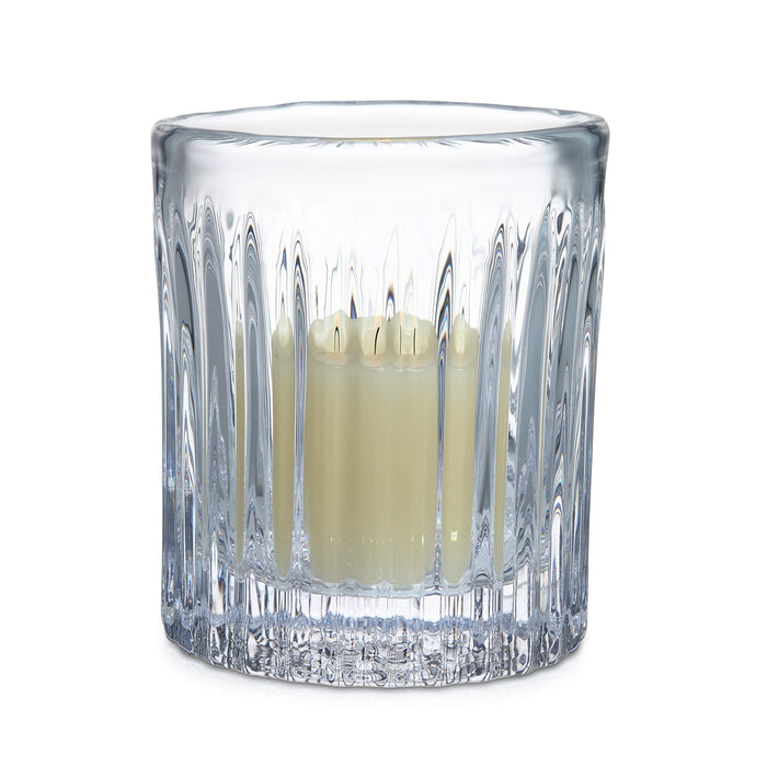 Clear crystal hurricane vase with vertical ribbed pattern holding lit cream-colored candle.