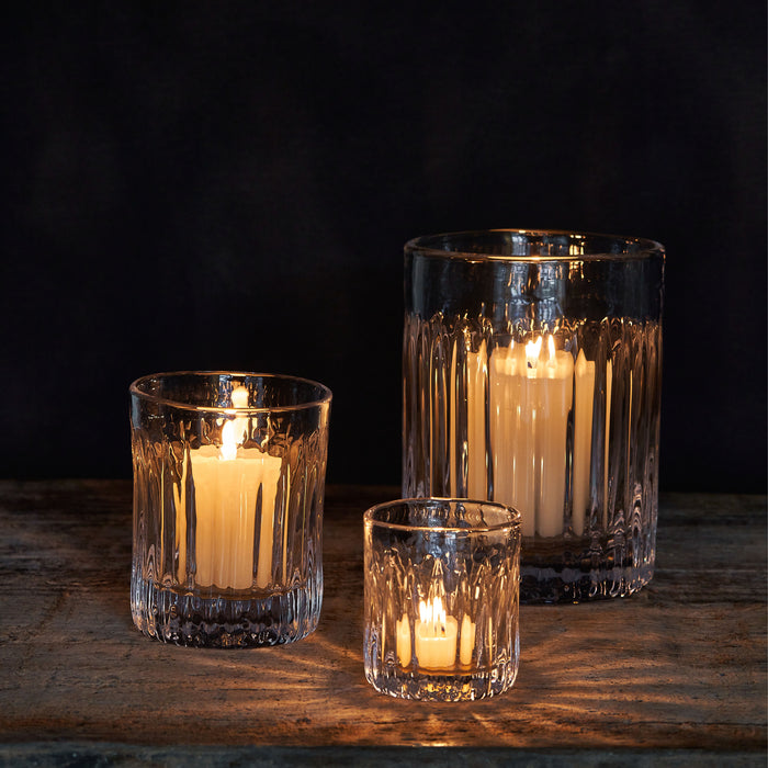 Three lit candles in textured glass holders of varying heights against a dark background.