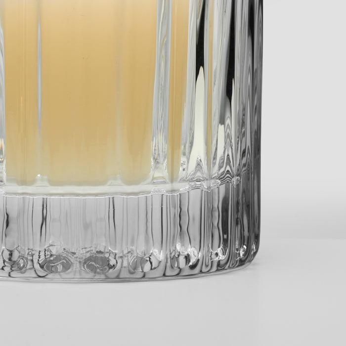 Clear glass hurricane with vertical ribbed texture and pale yellow liquid inside.