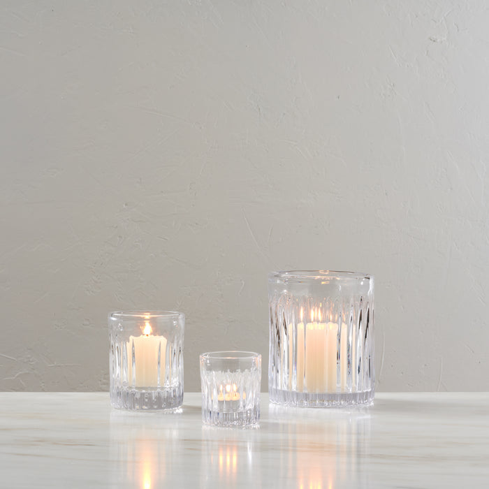 Three clear crystal tealight holders of varying heights with lit cream-colored candles inside.