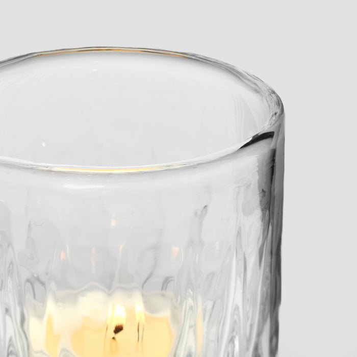 Clear glass tealight holder with gold rim and cream-colored wax candle inside.