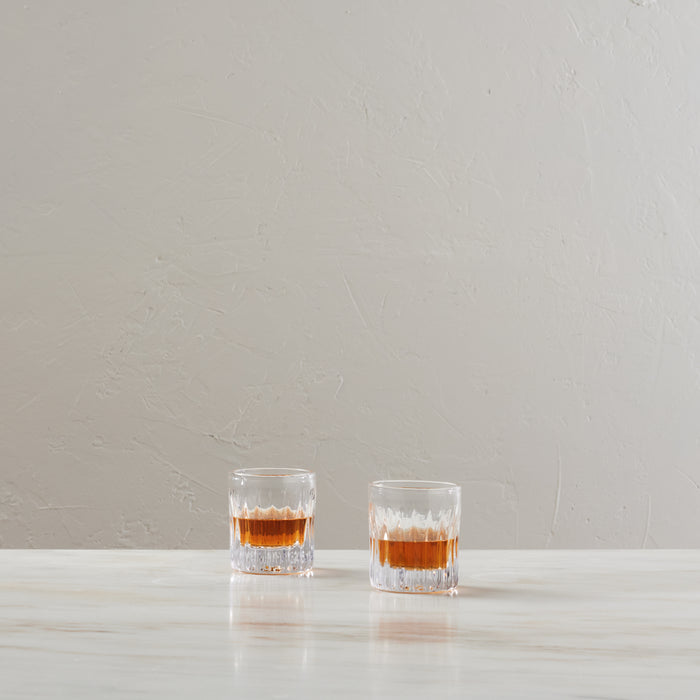 Two crystal whiskey glasses filled with amber liquid on a white surface.
