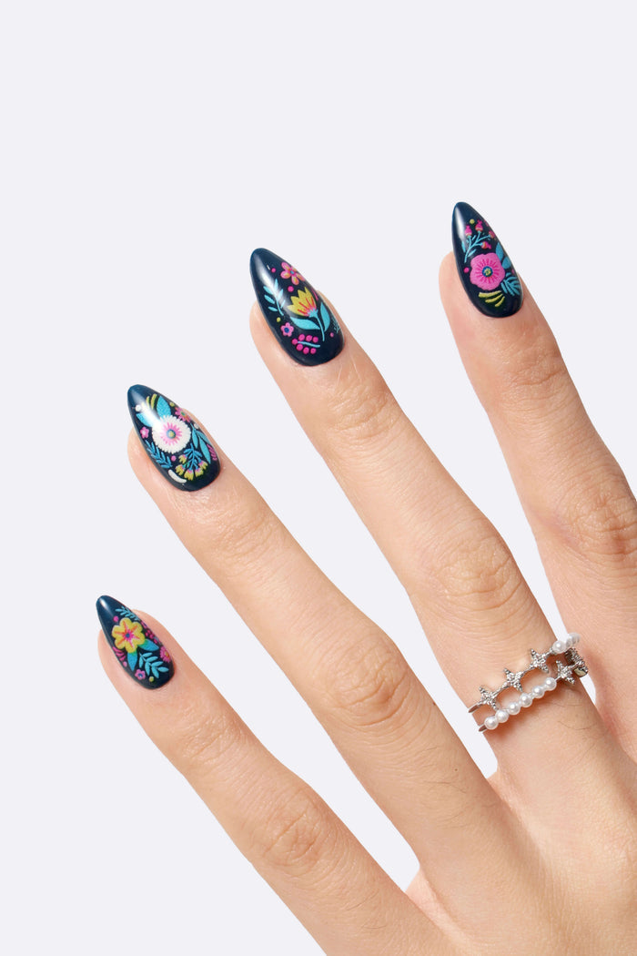 Dark blue stiletto press-on nails with colorful floral designs, including a pink poppy, yellow flowers, and blue leaves.