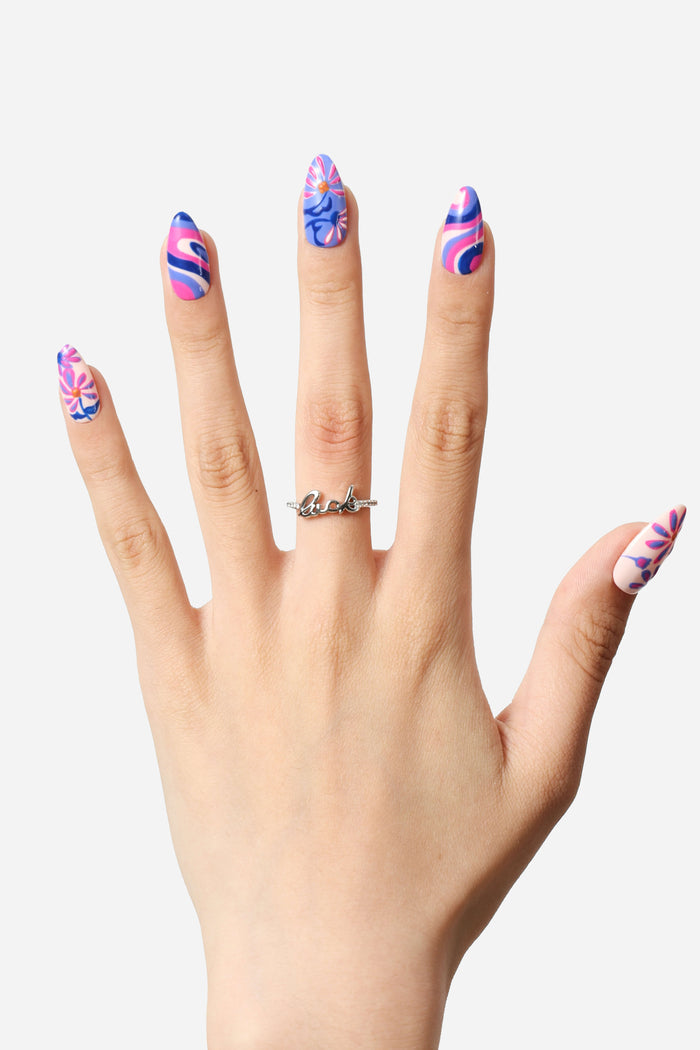 Hand with Mystic Daisy press-on nails by Jess Miller: floral & swirl designs in pink, blue, purple. Silver 'luck' ring.