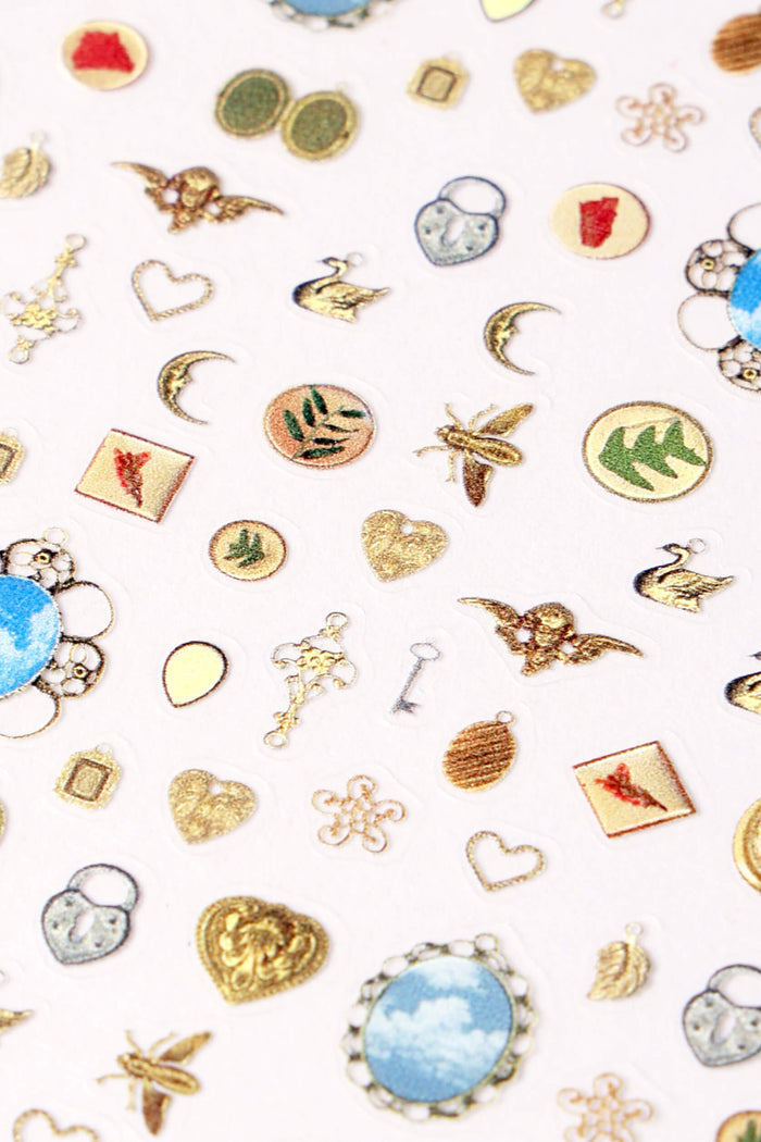 Sheet of assorted ornate nail stickers featuring gold hearts, keys, lockets, bees, swans, and celestial motifs.