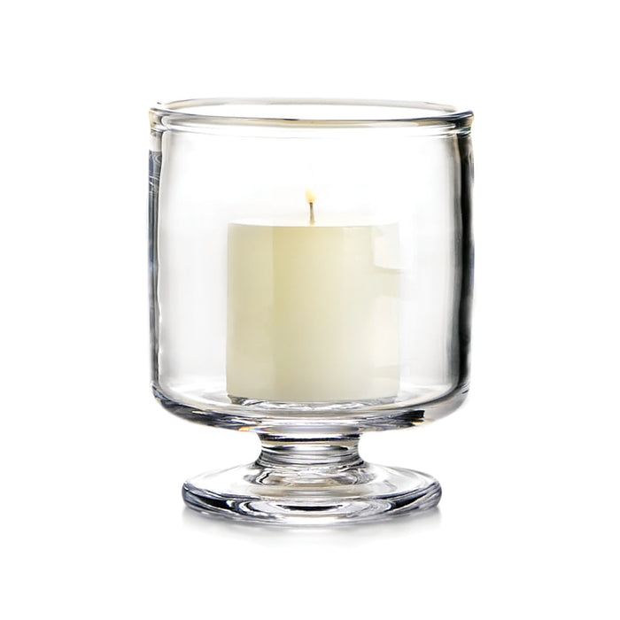 Cream-colored candle in a clear glass hurricane vase with pedestal base.