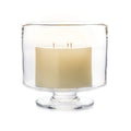 Cream-colored candle with two wicks inside a clear glass hurricane with pedestal base.