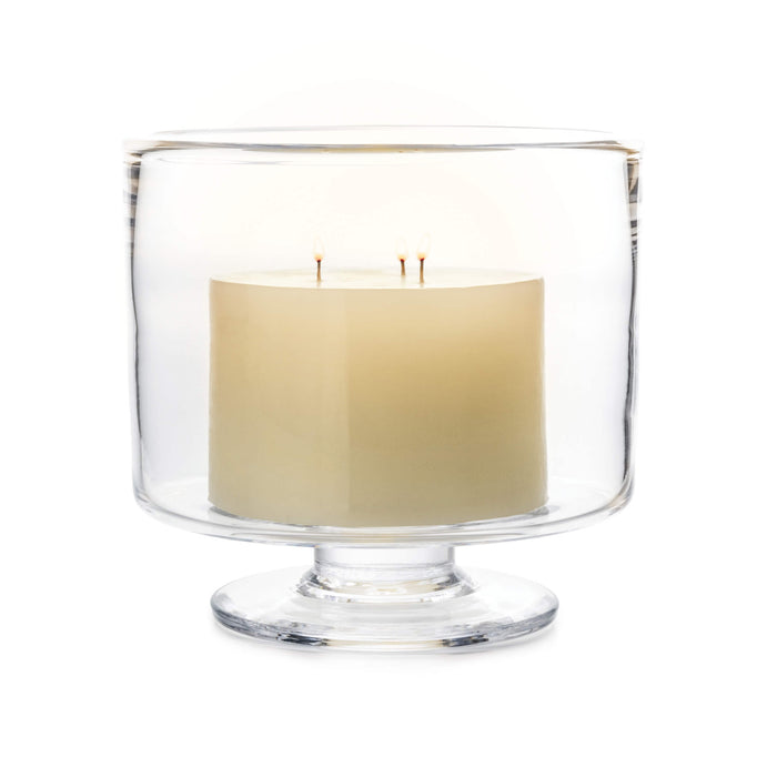 Cream-colored candle with two wicks inside a clear glass hurricane with pedestal base.