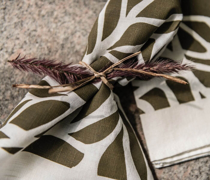 Two olive and white block print napkins with leaf design, tied with dried botanicals.