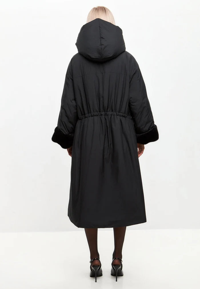 A stylish woman wearing an oversized black puffer coat with a hood, faux fur cuffs, and plus size fit, the perfect women's fashion jacket for winter.