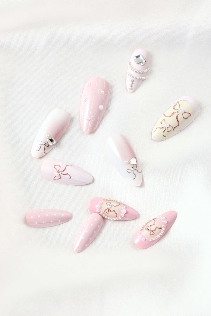 Almond press-on nails with painted bows and pearl accents in soft pink and white.