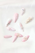 Almond press-on nails with painted bows and pearl accents in soft pink and white.