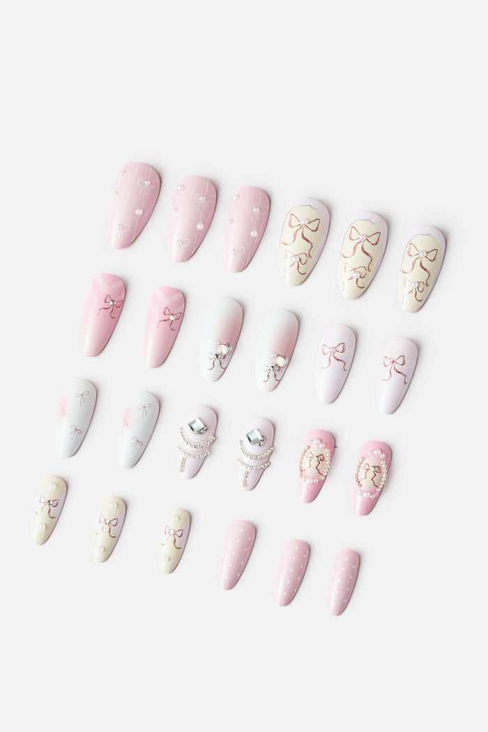 Almond press-on nails with delicate pink bows, pearls, and rhinestones on a white background.