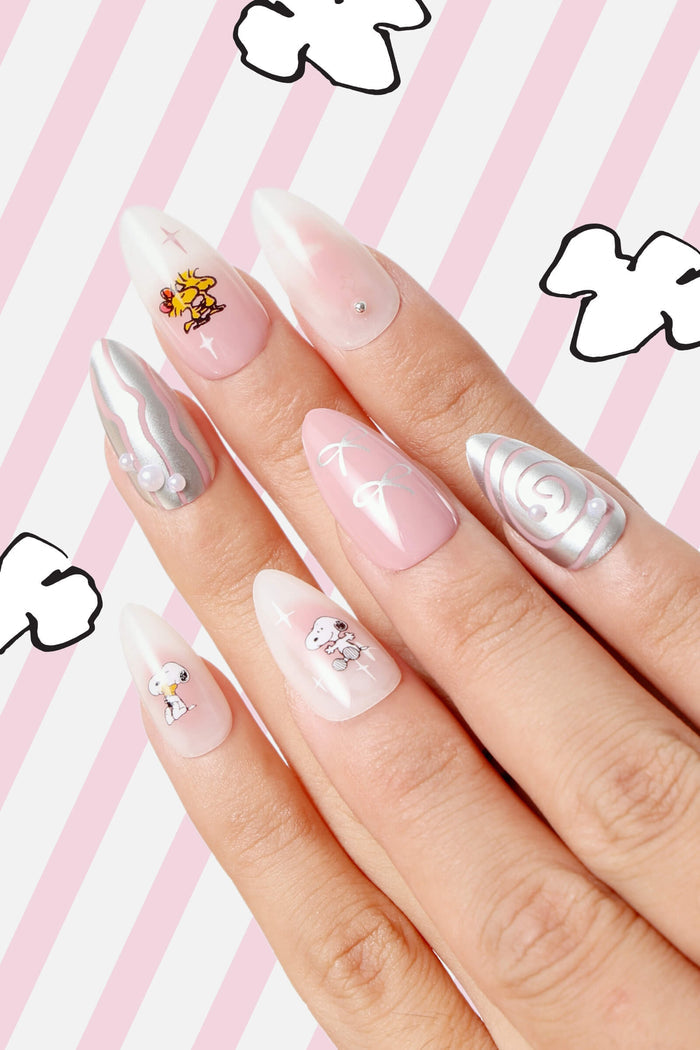 Almond press-on nails featuring Snoopy and Woodstock designs with pink and silver swirls, adorned with pearls and bows.