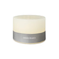 Ivory cylindrical pillow candle with three wicks and gray band label reading "Simon Pearce."